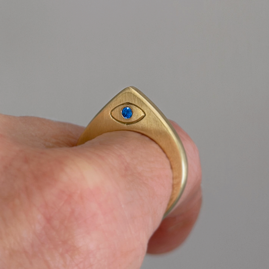 Brass ring with a blue gemstone on a finger against a gray background