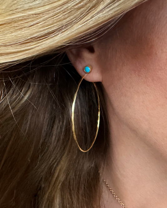 Close-up of a person wearing a golden hoop earring with a turquoise gemstone.