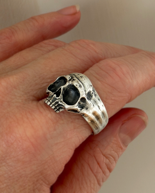 Silver skull ring on a person's finger with a plain background
