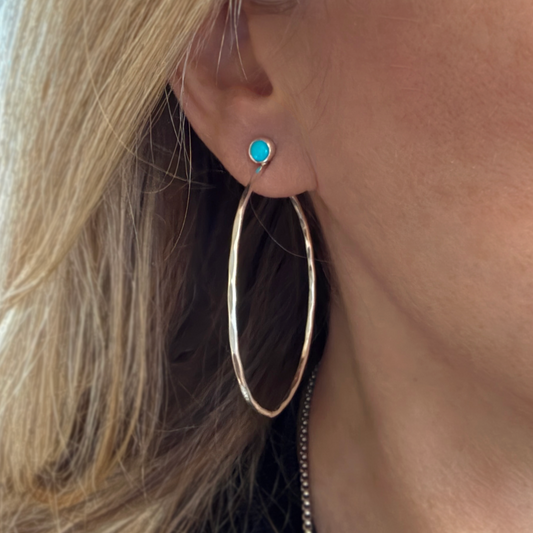 Close-up of a person wearing silver hoop earrings with turquoise.