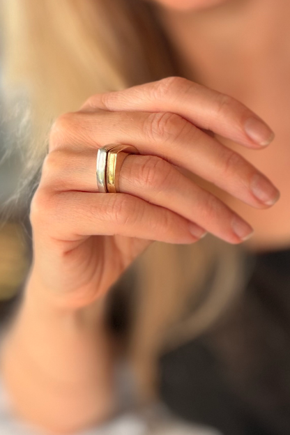 A close-up of a person's hand wearing two slim bands: one silver band and one gold band.