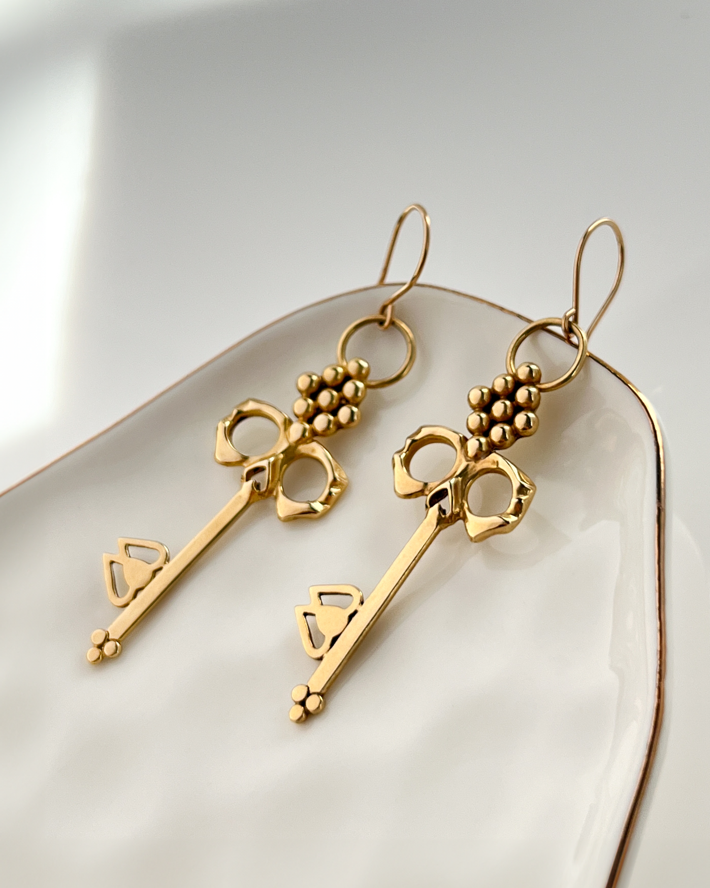 Brass Skull Key Earrings that dangle from 14K gold-filled hypoallergenic handmade French hooks on jewelry dish