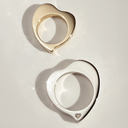 Two heart-shaped metal rings, one in polished gold and one in polished silver, displayed on a clean white surface with soft shadows.
