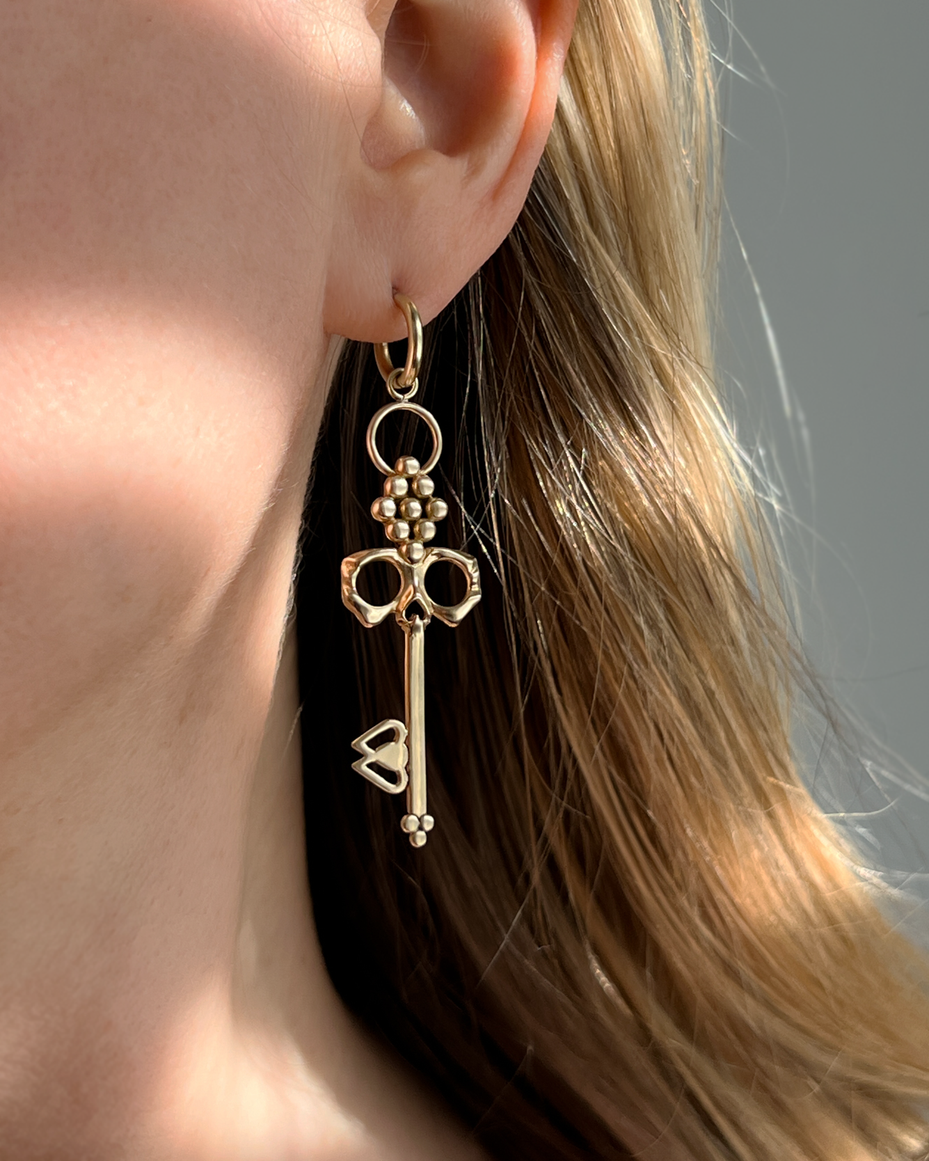 Brass Skull Key Earrings that hang from small detachable Huggie Hoops shown dangling from ear