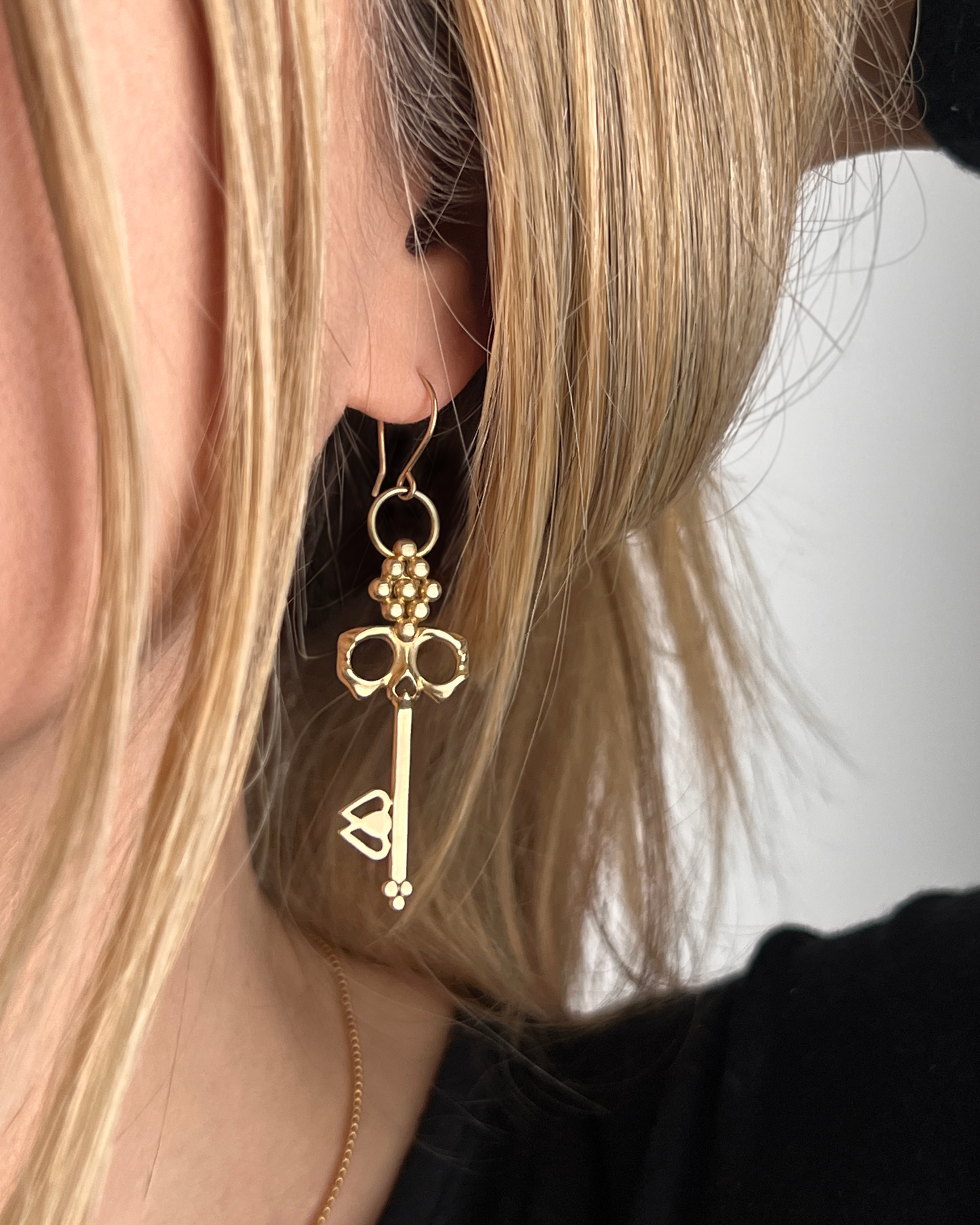 Brass Skull Key Earrings that dangle from 14K gold-filled hypoallergenic handmade French hooks are shown on ear