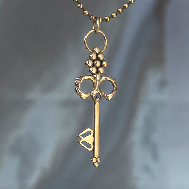 Men's Brass Skull Key Necklace hung from durable ball chain suspended with ethereal backdrop