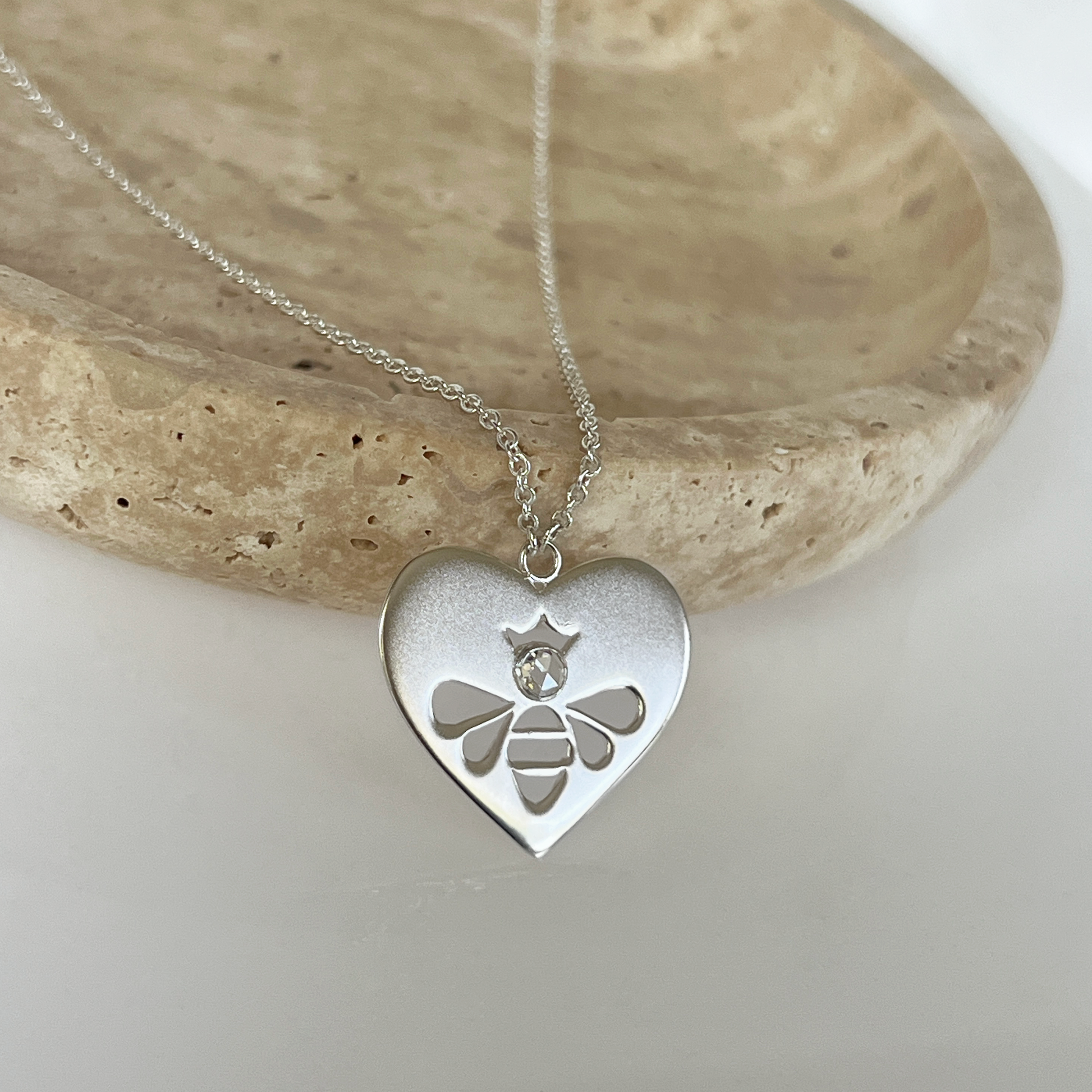 Queen Honey Bee cutout in sterling silver heart medallion necklace with round rose cut white topaz draped over jewelry dish