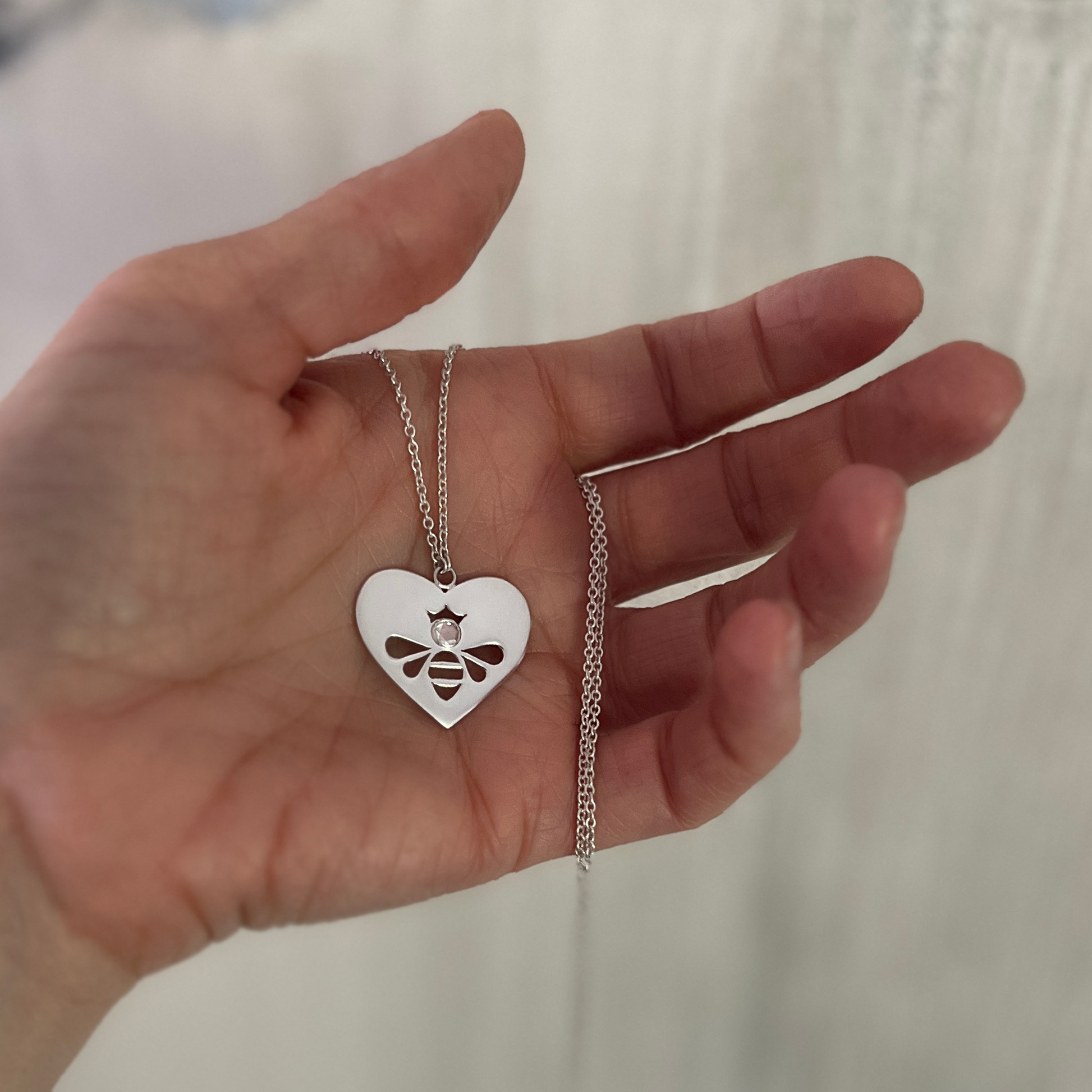 Queen Honey Bee cutout in sterling silver heart medallion necklace with round rose cut white topaz held in hand