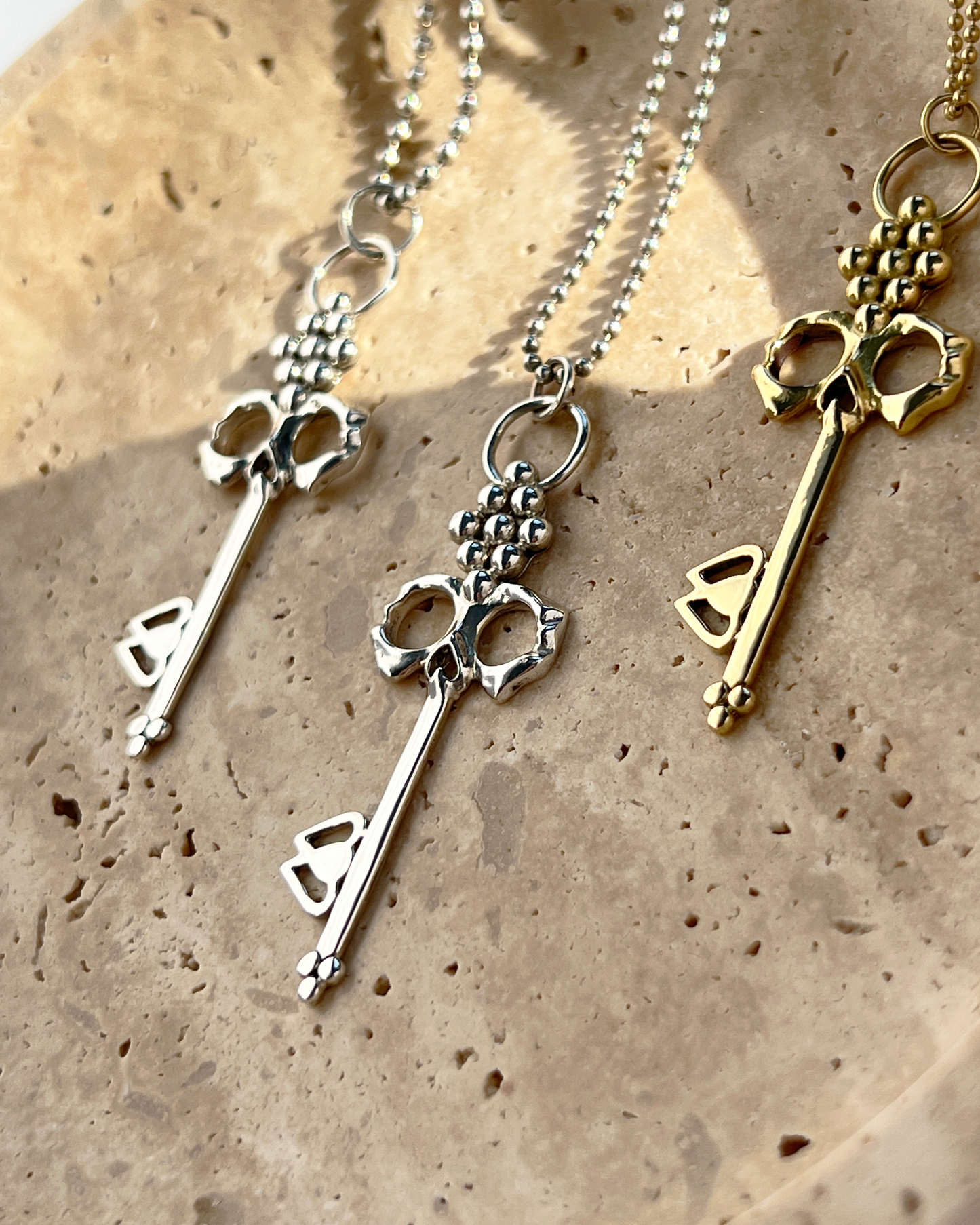 Sterling Silver Skull Key Necklaces shown with other jewelry on natural jewelry dish