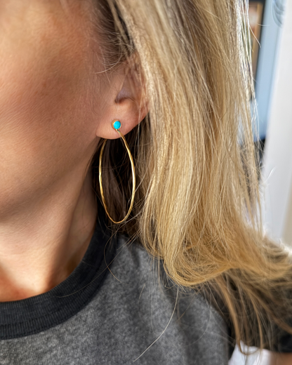 Close-up of a person wearing golden hoop earrings with turquoise.
