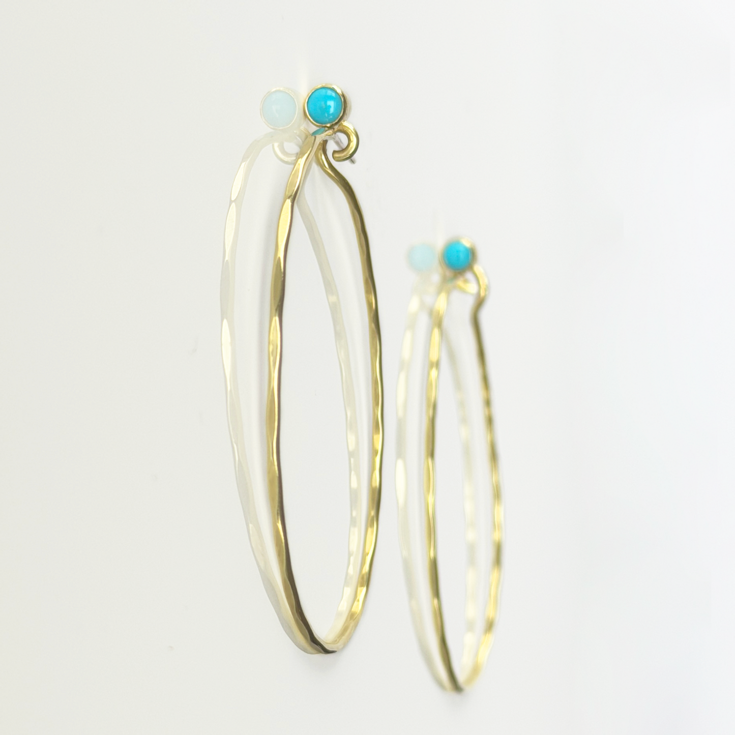 Golden, hammered hoop earrings with turquoise stones on a white background