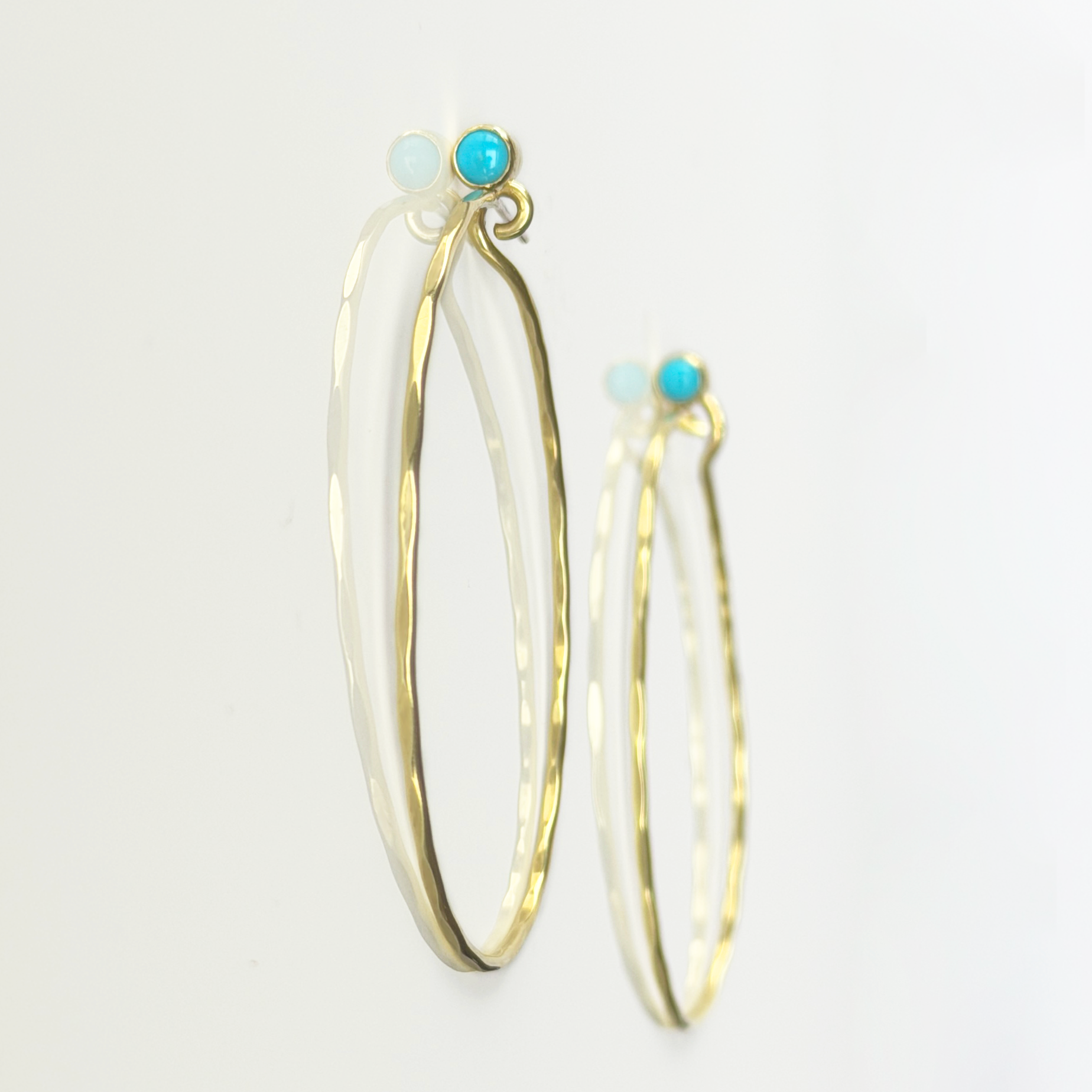 Golden, hammered hoop earrings with turquoise stones on a white background