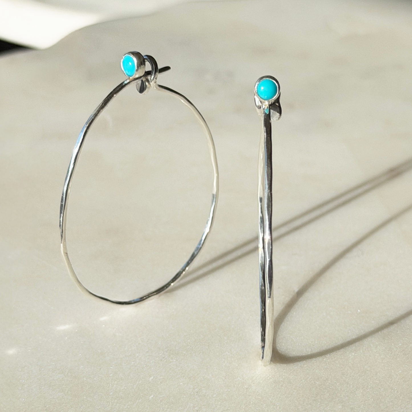 Silver hoop earrings with turquoise stones on a light background