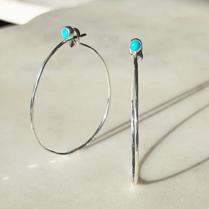 Silver hoop earrings with turquoise stones on a light background