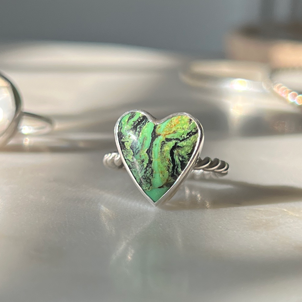 Green turquoise heart ring on jewelry dish, sparkling in sun.