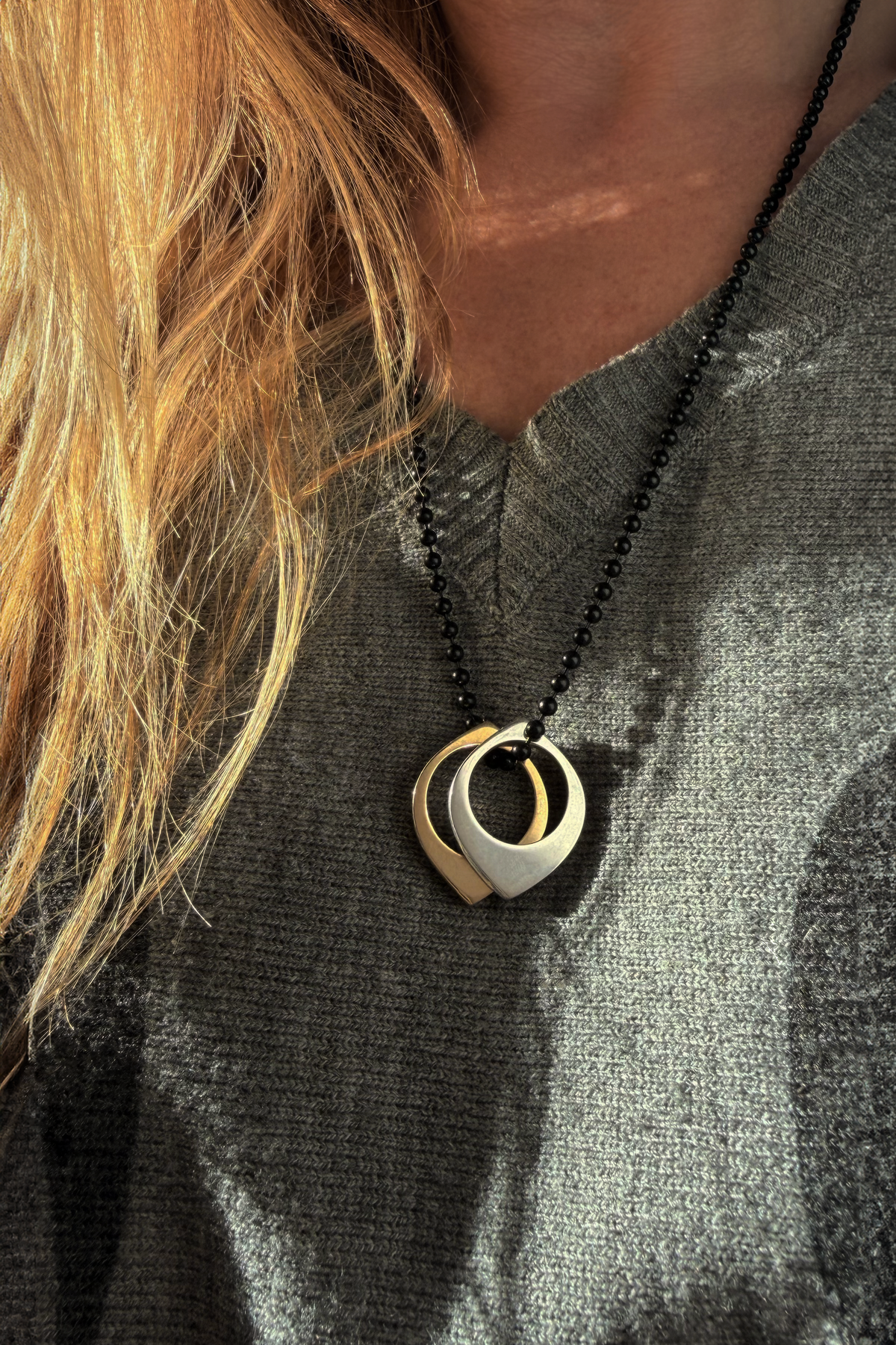 A close-up of a person wearing two Oracle Slice Rings as pendants on a black beaded chain, one in silver and one in brass.
