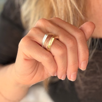 Close-up of two shiny bands worn together on a finger, one silver and one gold.