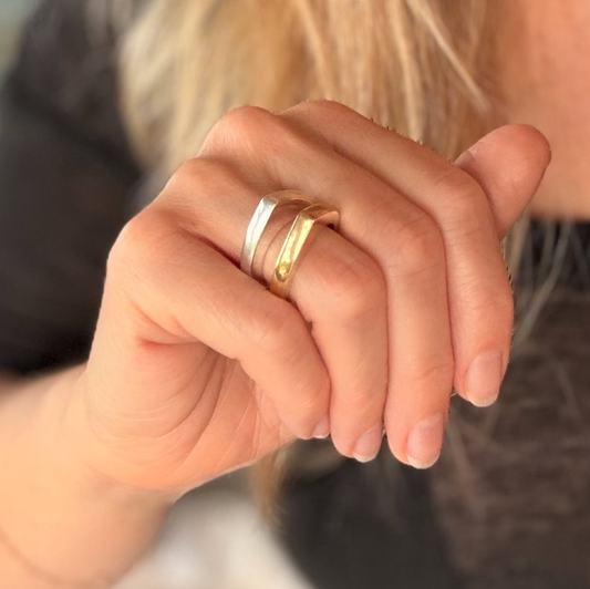 Close-up of two shiny bands worn together on a finger, one silver and one gold.