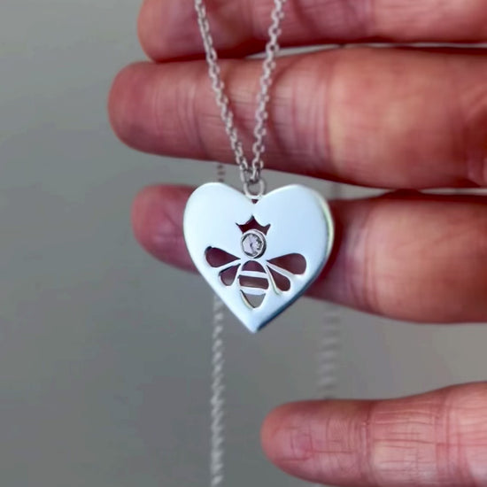 Queen Honey Bee cutout in sterling silver heart medallion necklace with round rose cut white topaz, swaying slightly as it is draped over fingers, reflecting light and illuminating stone.