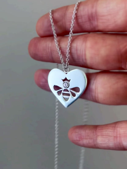 Queen Honey Bee cutout in sterling silver heart medallion necklace with round rose cut white topaz, swaying slightly as it is draped over fingers, reflecting light and illuminating stone.