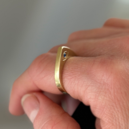 Brass ring with a blue gemstone on a finger against a neutral background